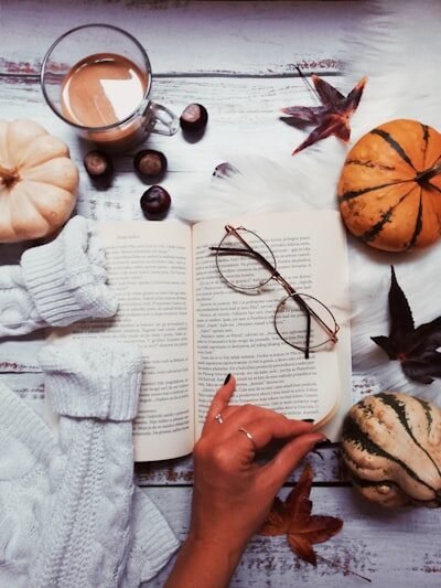 woman about to turn the page surrounded with gourds and glass of coffee