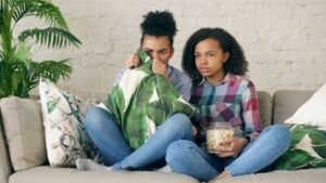 Two people watching tv, one holding popcorn.