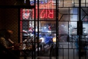 a man sitting at a table in front of a neon sign