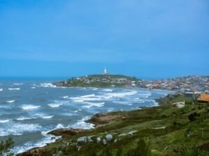 Coastal town with lighthouse on a hill overlooking ocean.