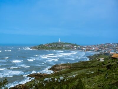 Coastal town with lighthouse on a hill overlooking ocean.