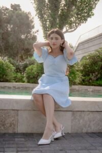 Young woman in blue dress sits by fountain