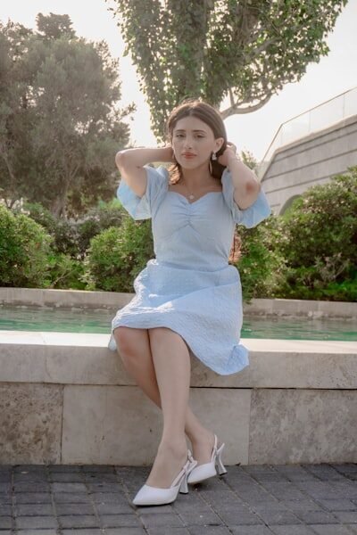 Young woman in blue dress sits by fountain